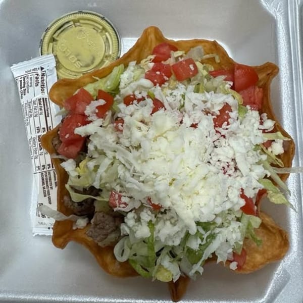 A taco salad in a crispy fried shell, topped with lettuce, tomatoes, and shredded white cheese.