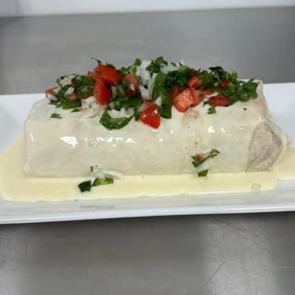 A large burrito covered in white sauce, topped with diced tomatoes, onions, and cilantro.