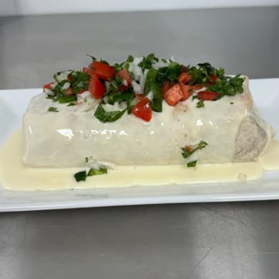 A large burrito covered in white sauce, topped with diced tomatoes, onions, and cilantro.