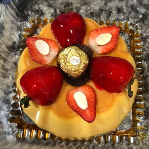 Flan dessert topped with fresh strawberries and a gold-wrapped chocolate candy.