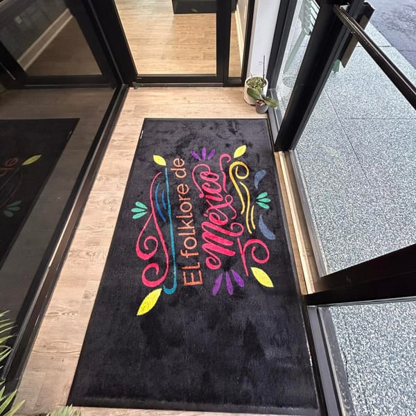 A black welcome mat with "El Folklore de Mexico" in colorful script at a restaurant entrance.