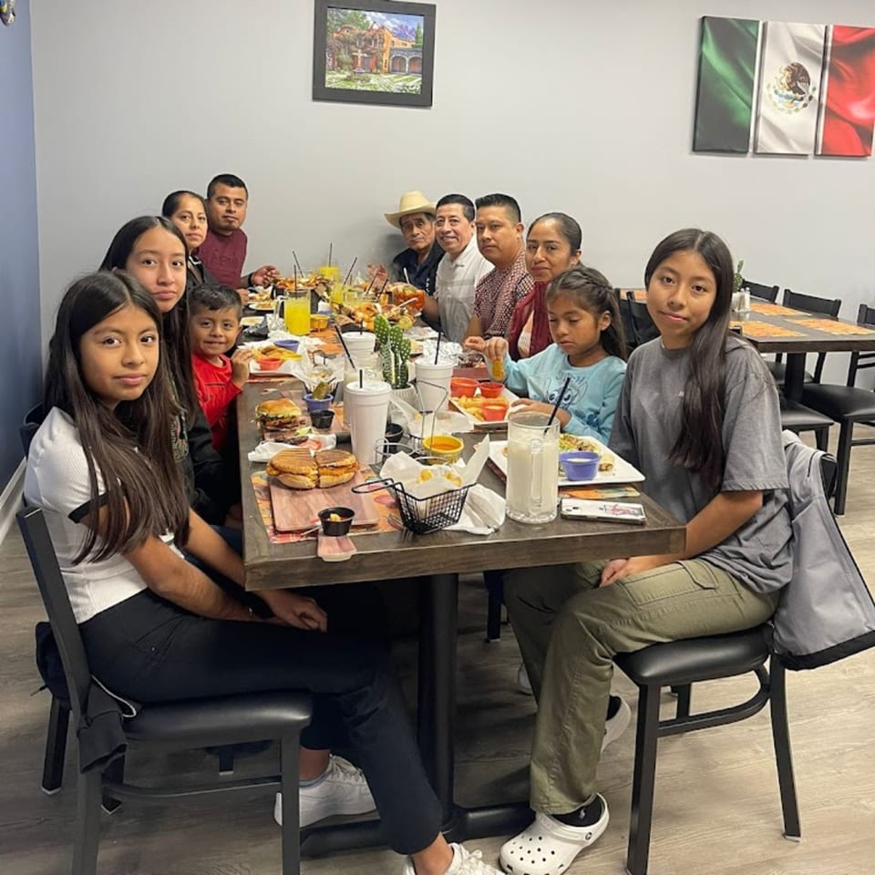 A large family group, including children, enjoys a meal together at a long table in a Mexican restaurant.