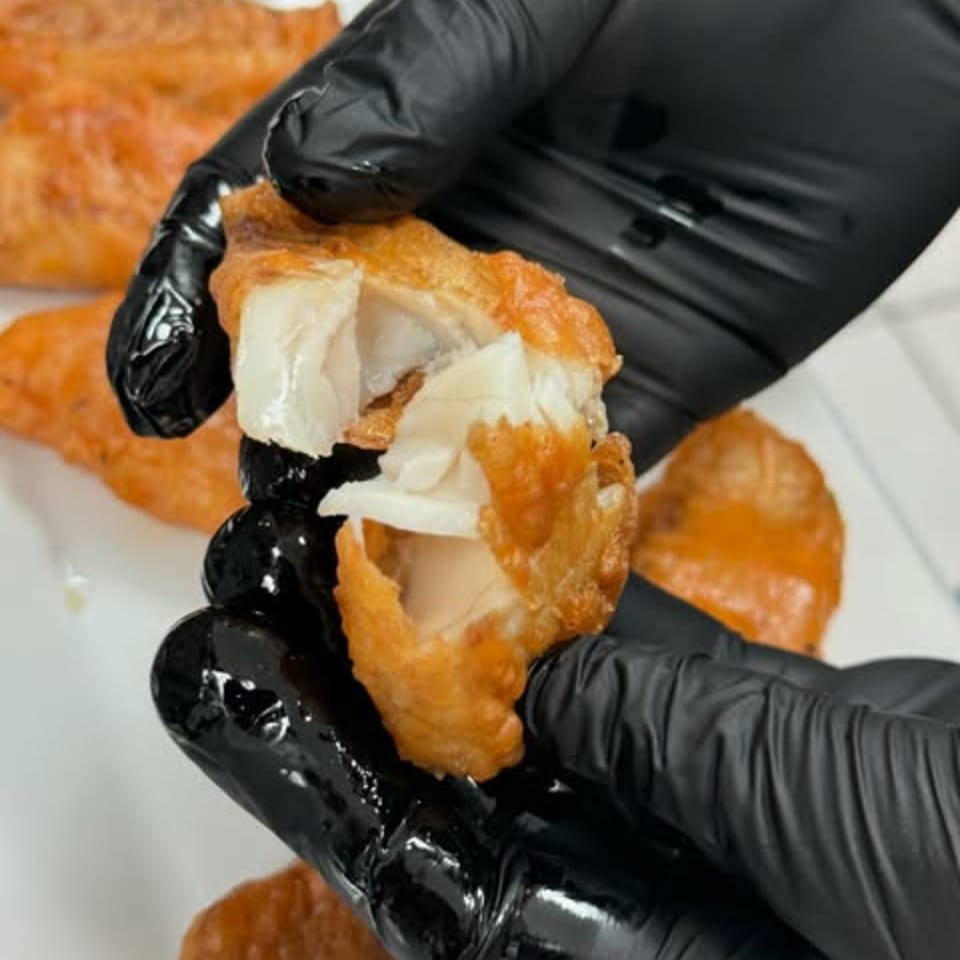 Gloved hands breaking open a piece of crispy fried fish, revealing its flaky white interior.