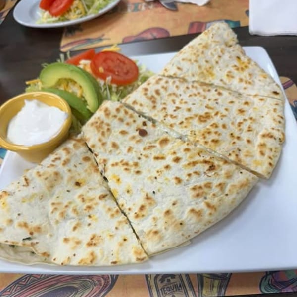 A cheese quesadilla cut into triangles, served with sour cream, avocado, and salad.