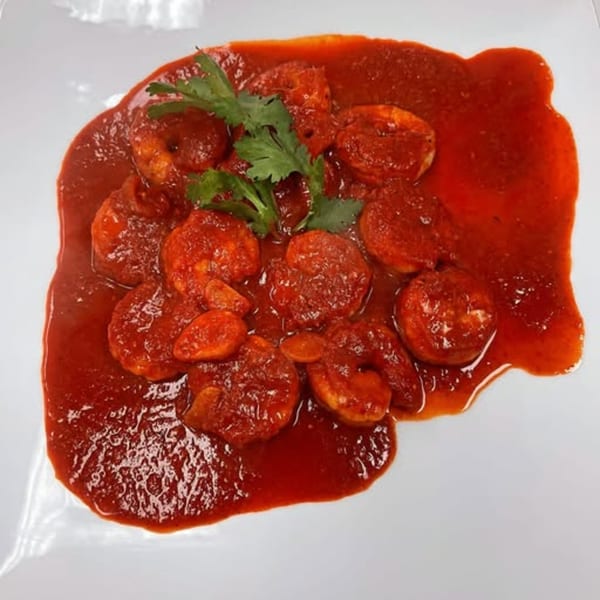 Shrimp in a rich red sauce, garnished with fresh cilantro, served on a white plate.
