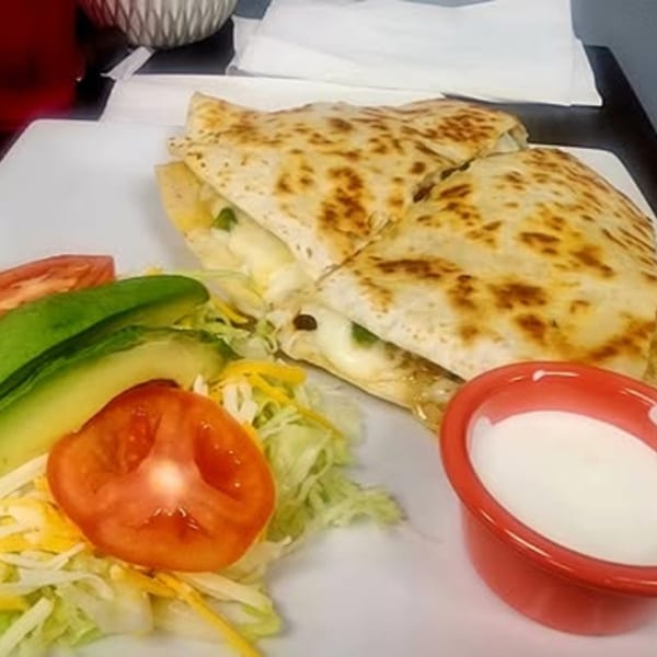 A cheese quesadilla with avocado, tomato, lettuce, and a side of sour cream on a white plate.