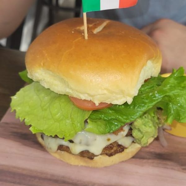 A Mexican burger with guacamole, cheese, lettuce, and tomato, topped with an Italian flag toothpick.