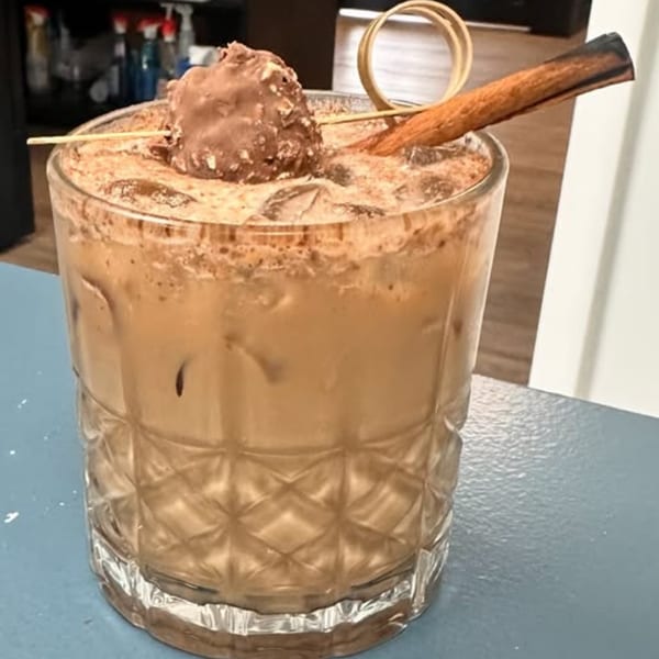 Mexican horchata cocktail in a patterned glass, garnished with a chocolate truffle and cinnamon stick.